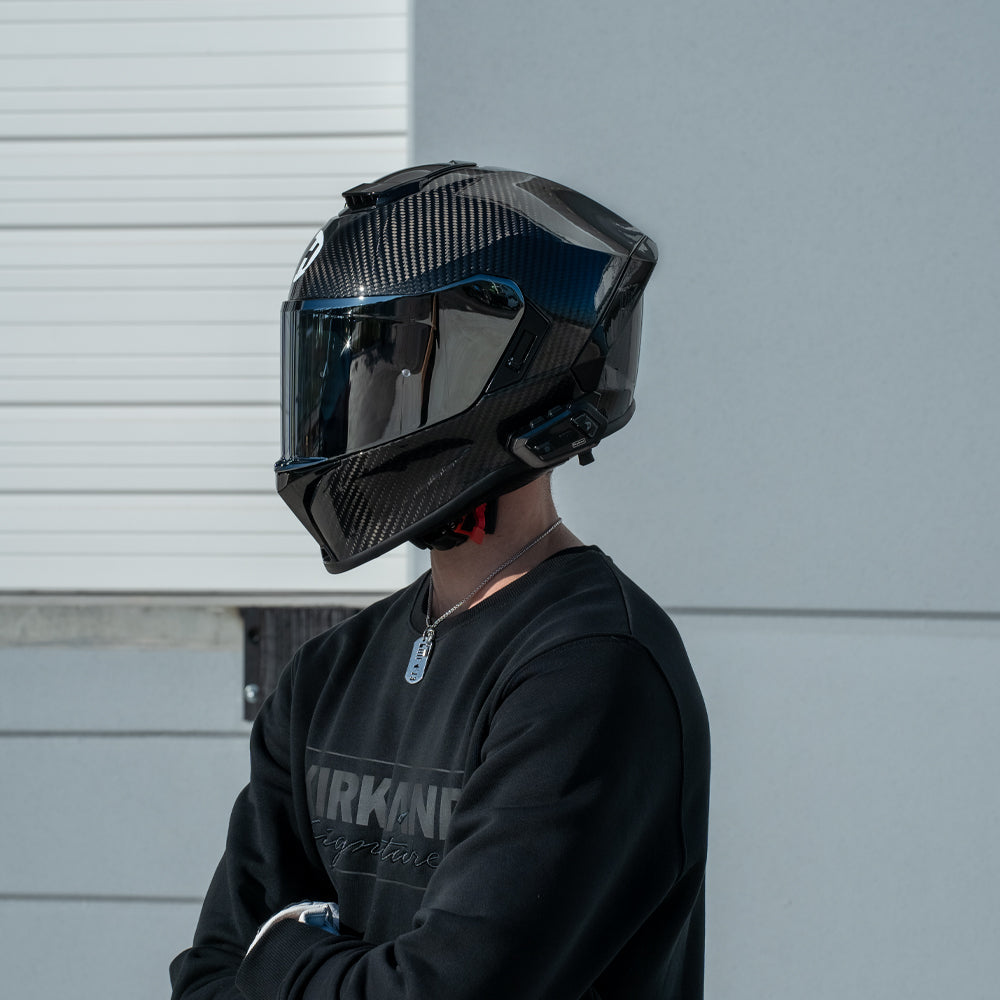Person wearing a black motorcycle helmet with a reflective visor against a light gray background