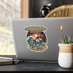 Laptop with a Daytona Bike Week sticker on a desk with a plant and pen.