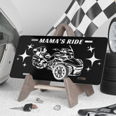Black license plate with car design and 'Mama's Ride' text, placed on a stand with tools and tires in the background.