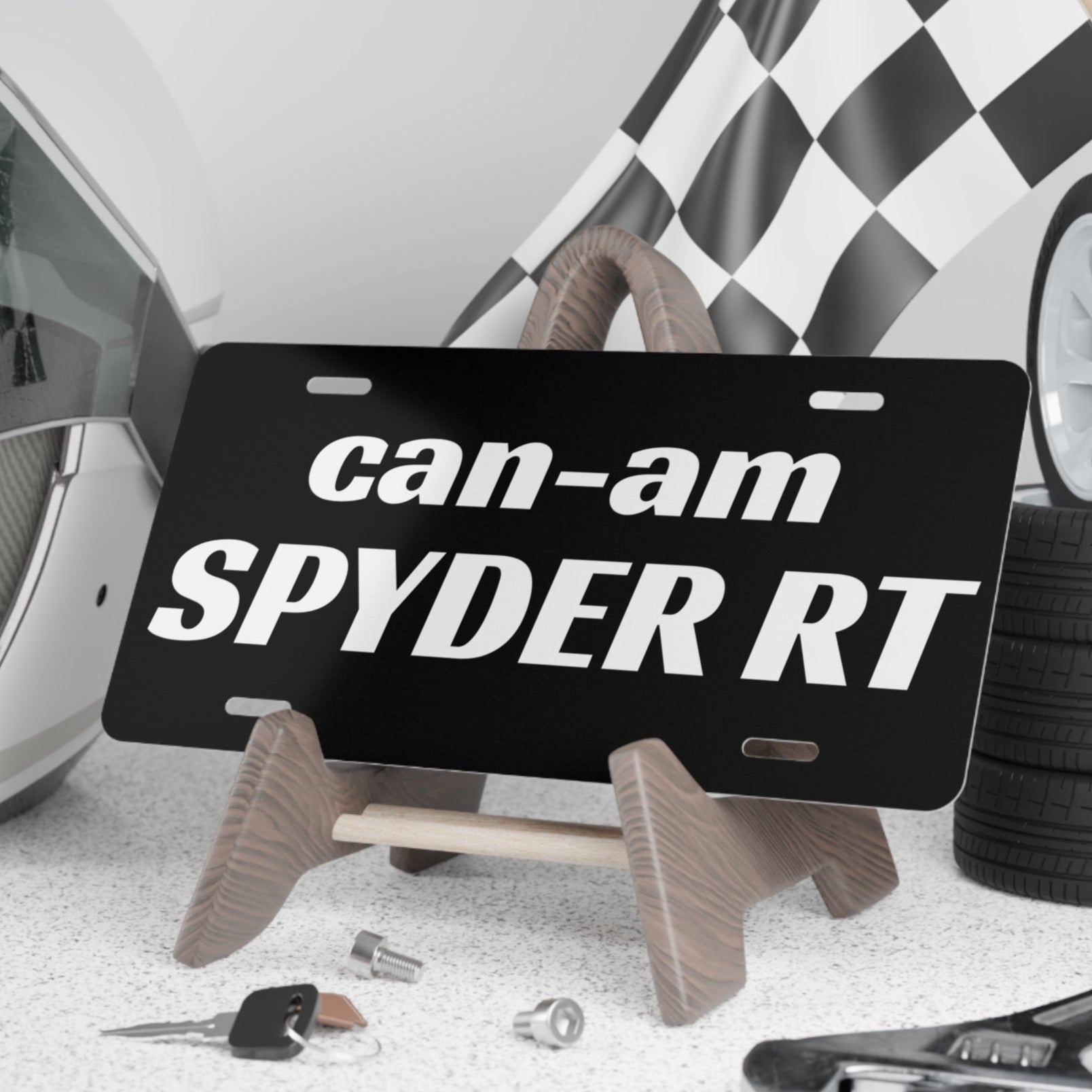 Can-Am Spyder RT license plate on a stand with helmet, tools, and checkered flag in the background.