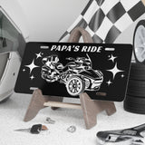 Black license plate with car design and 'Papa's Ride' text, placed on a stand with tools and tires in the background.