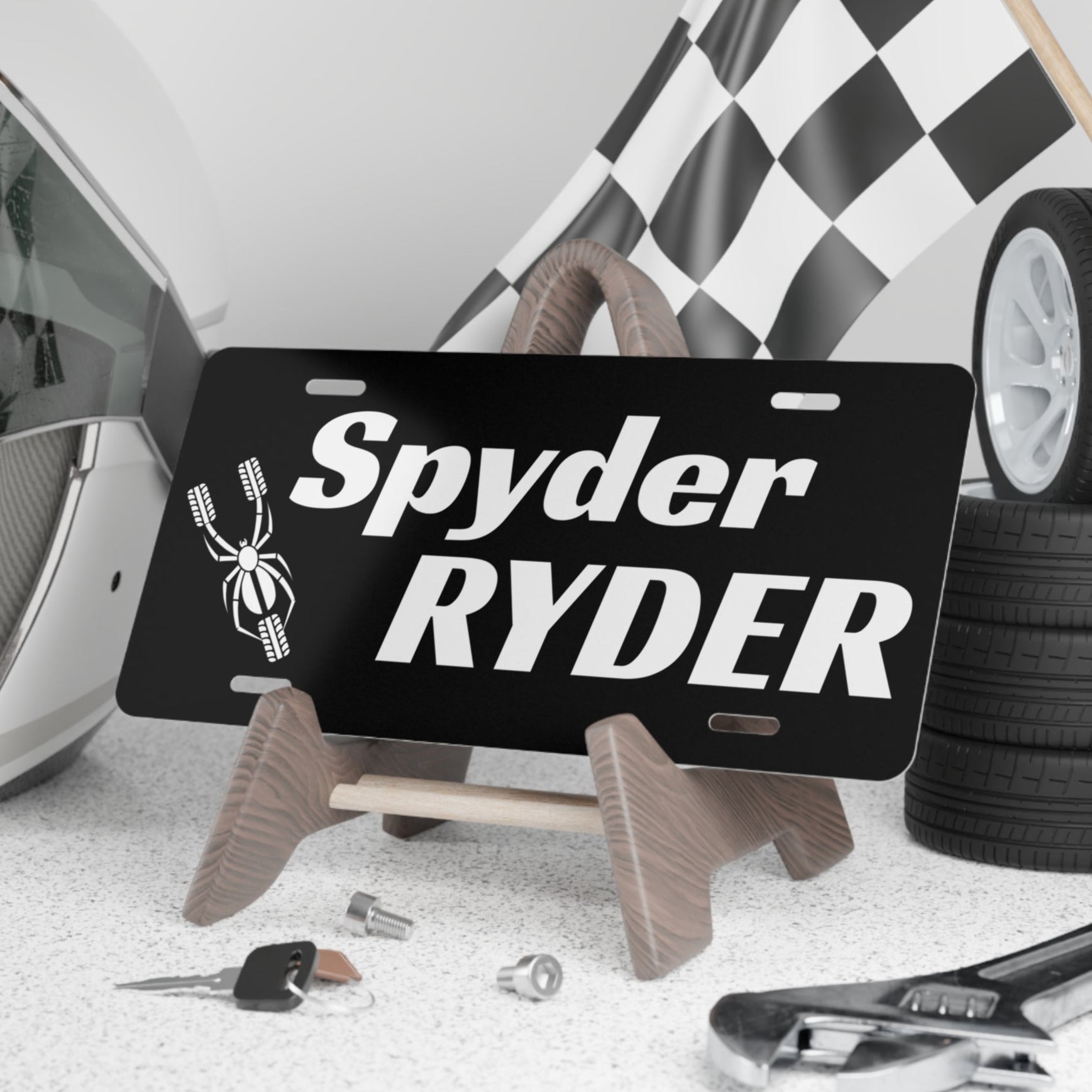 Black license plate with 'Spyder Ryder' text on a stand, surrounded by automotive items.