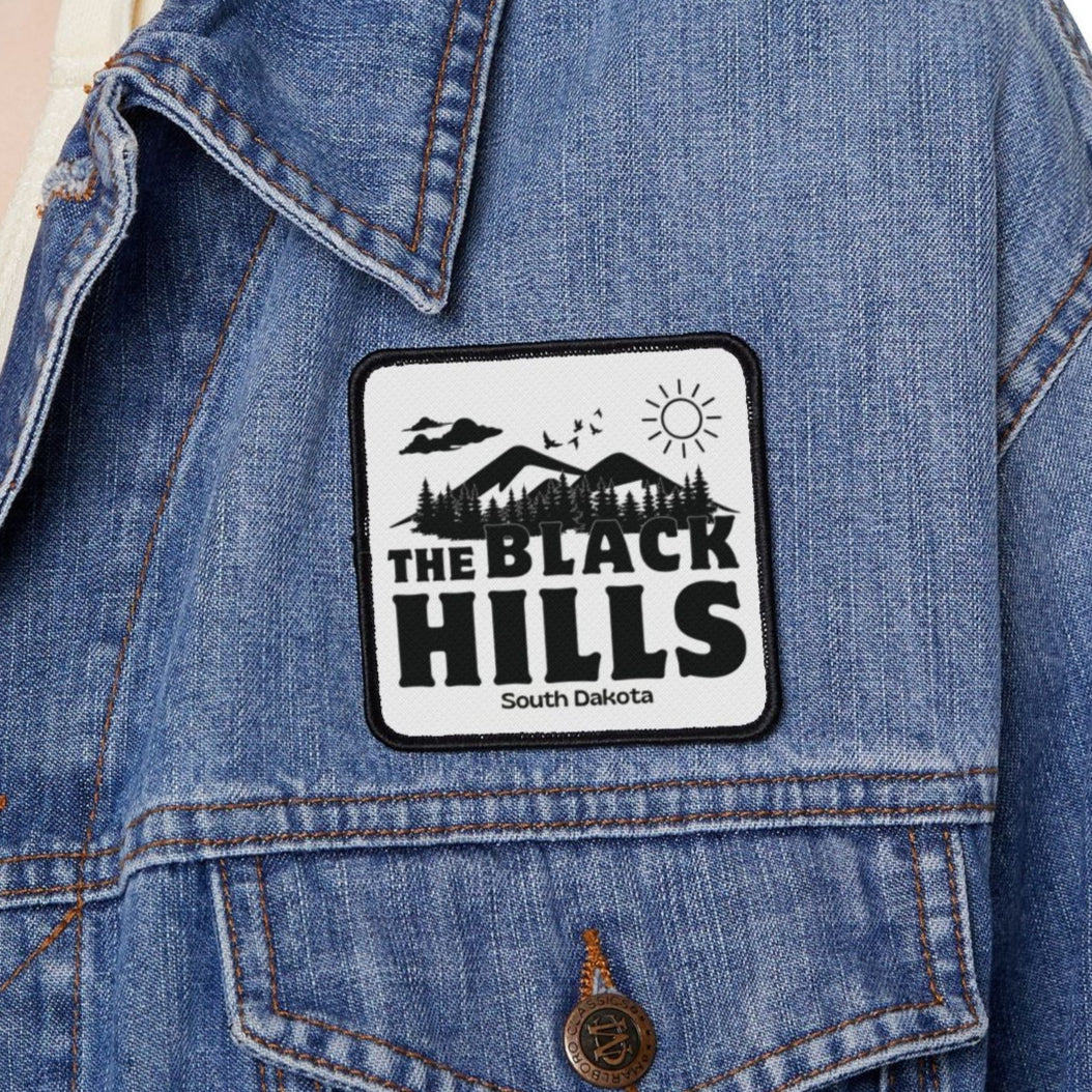 Person wearing a denim jacket with a 'The Black Hills' patch on a white background