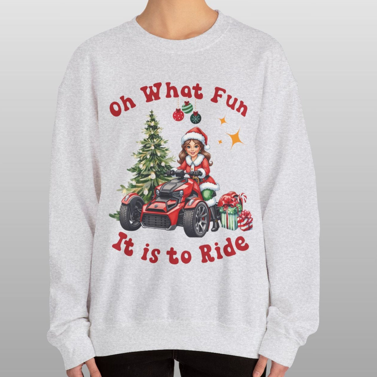 Person wearing a Christmas-themed sweatshirt with a design of a child in a Santa hat driving a red vehicle near a Christmas tree, with text 'Oh What Fun It is to Ride'.