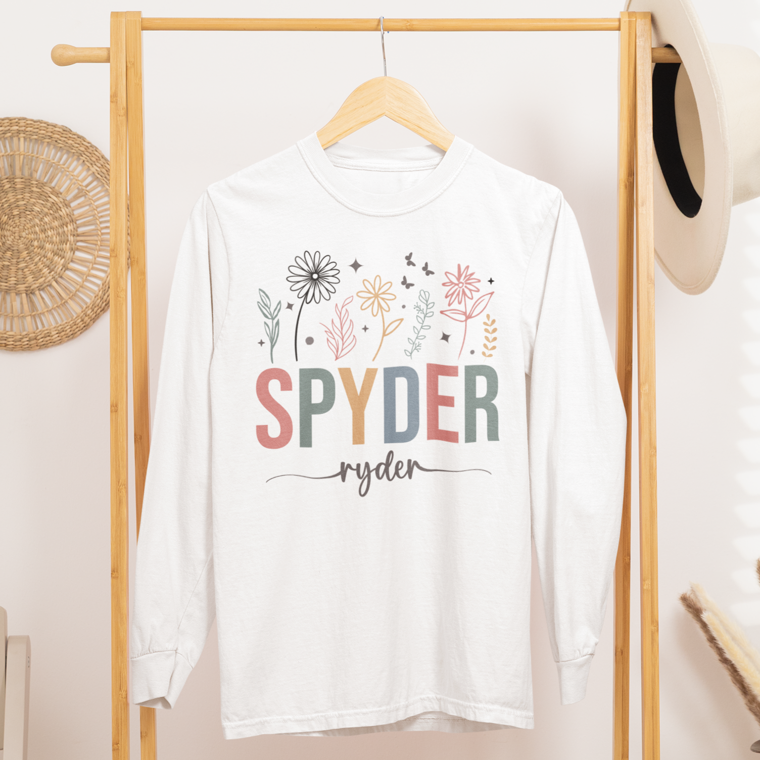 White t-shirt with colorful text and graphics on a wooden rack in a room.