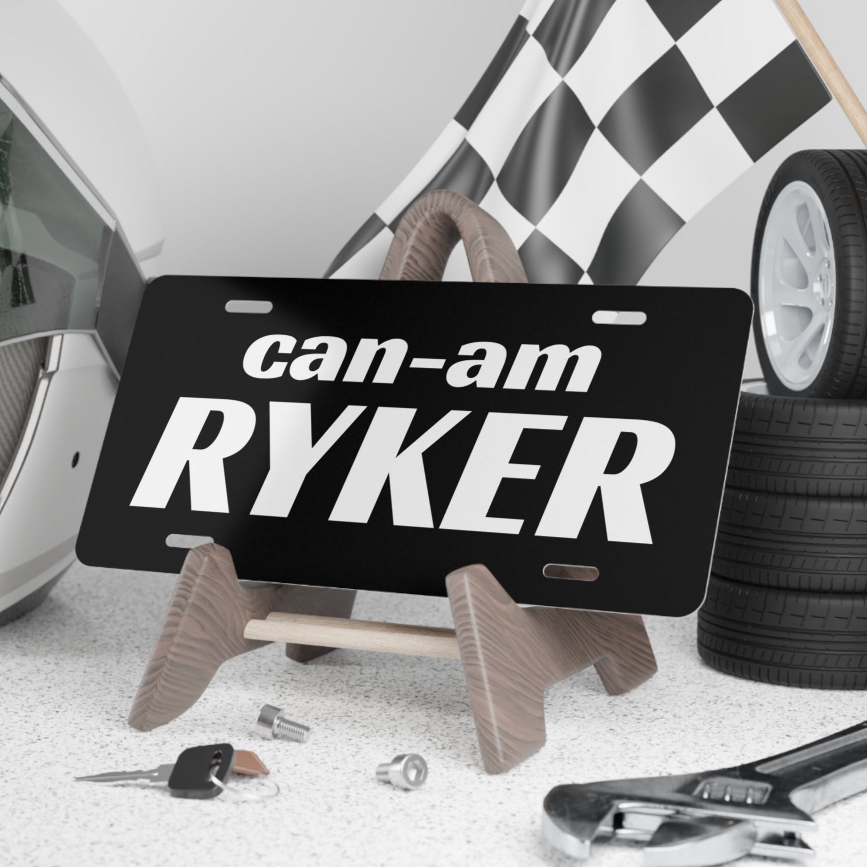 Can-Am Ryker license plate on a stand with a helmet, checkered flag, and tires in the background.