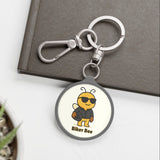 Keychain with a bee design labeled 'Biker Bee' on a white surface with a plant and book in the background.