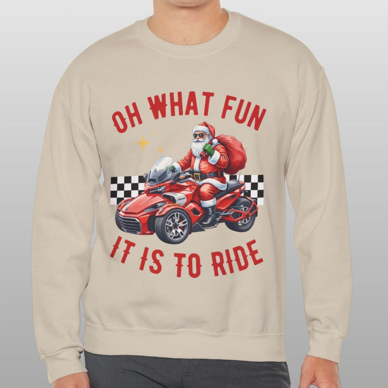 Man wearing a beige sweatshirt with a graphic of Santa driving a car and text 'OH WHAT FUN IT IS TO RIDE' on a plain background.