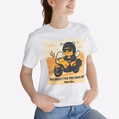 Person wearing a white t-shirt with a graphic design of a bee on a motorcycle, sitting in a room with a plant.