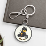 Keychain with a bee on a motorcycle design on a white surface with a plant and book in the background.