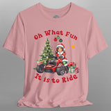 Pink t-shirt with Christmas-themed design featuring a child on a bike with trees and presents, on a gray background.