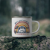 White mug with text and rainbow design on a tree stump in a forest setting