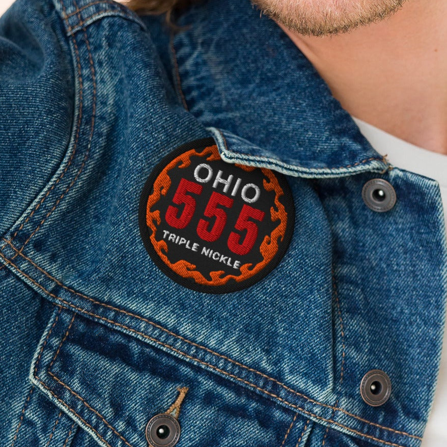 Man wearing a denim jacket with a patch on a plain background
