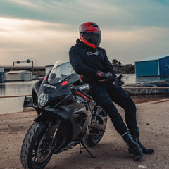 Person sitting on a Suzuki motorcycle by a waterfront with a red helmet