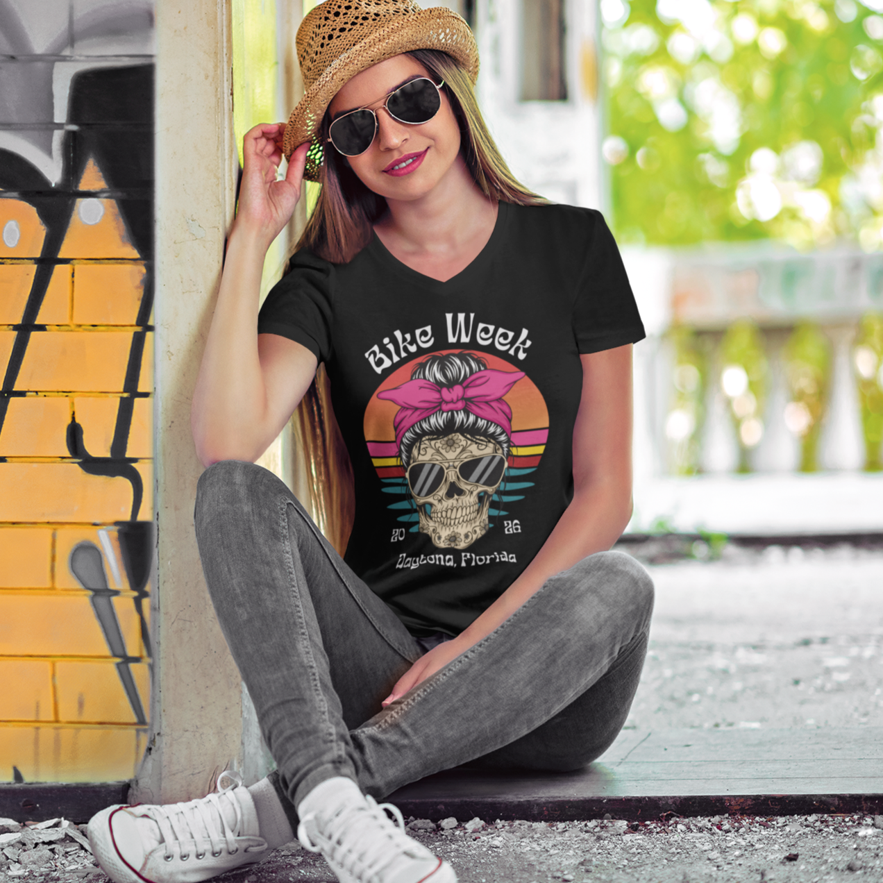 Woman wearing a black t-shirt with a graphic design, sitting against a colorful wall.