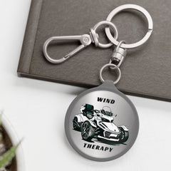 A silver acrylic keychain featuring a hand-drawn image of a Can-Am Spyder motorcycle with the text 'WIND THERAPY' on a metallic silver background.