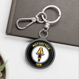 Keychain with 'Motorcycle Inn' logo on a white surface with a plant and book in the background