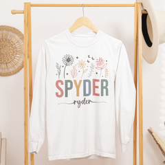 White t-shirt with colorful text and graphics on a wooden rack in a room.