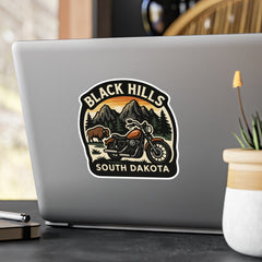 Laptop with a 'Black Hills South Dakota' sticker on a desk with a plant and pen.