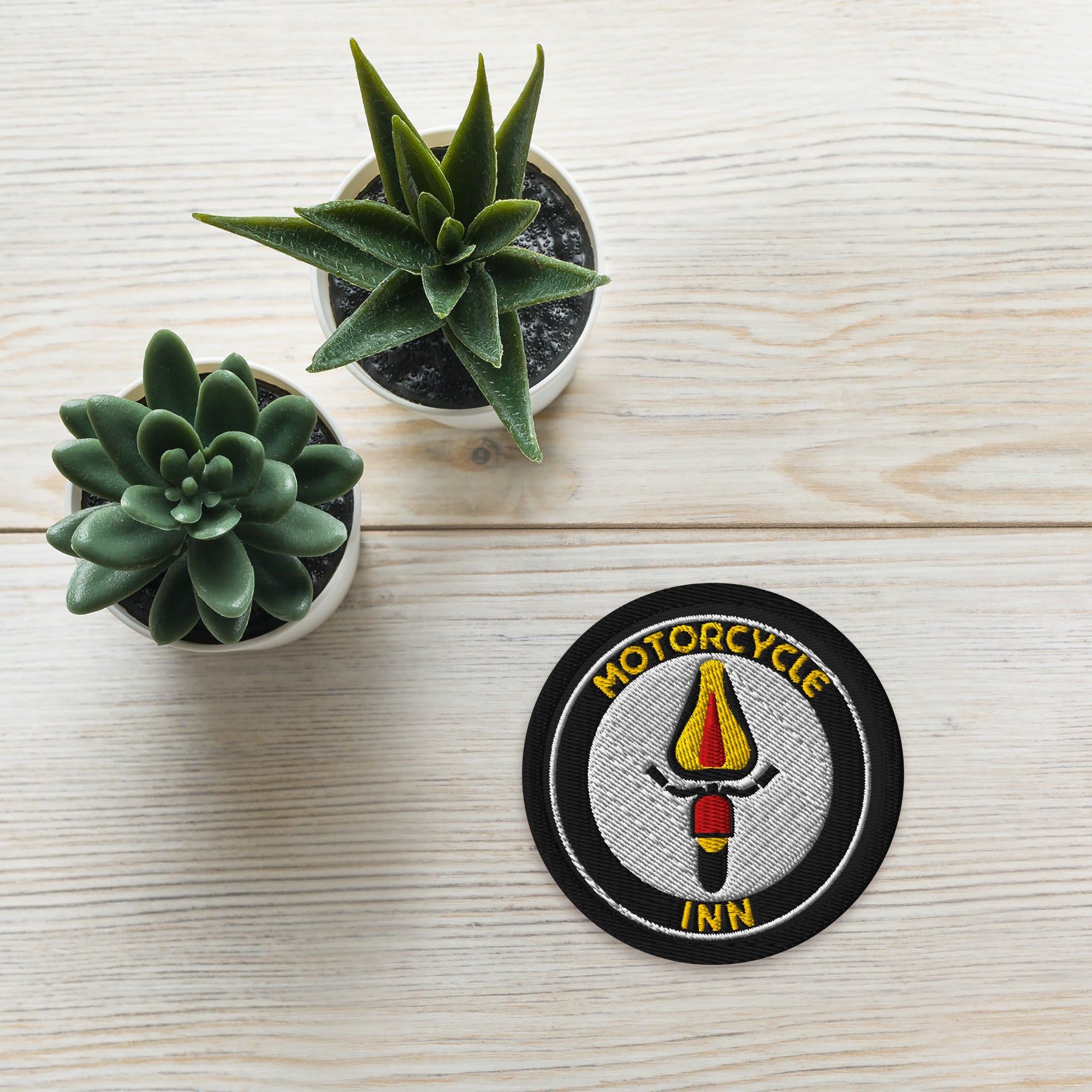 Motorcycle Inn patch on a wooden surface with two small potted succulents.