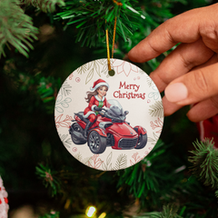 Hand holding a Christmas ornament with a Santa Claus riding a ATV design, surrounded by a decorated Christmas tree.