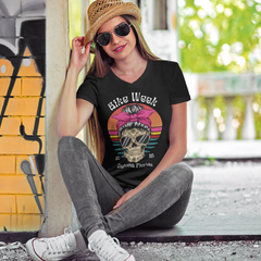 Woman wearing a black t-shirt with a graphic design, sitting against a colorful wall.